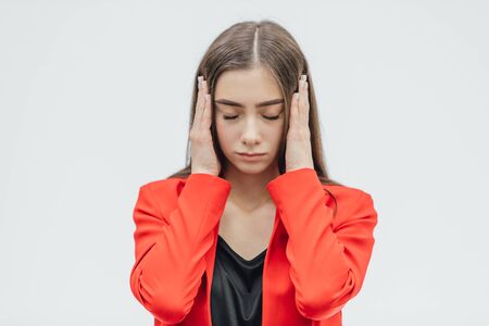 Portrait of a beautiful young brunette with open shoulders, touching her temples feeling stress, on a gray background.の写真素材