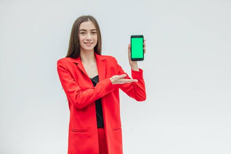 Young pretty pretty girl wearing a red jacket. Stays on a gray background. During this time, holds a black phone. Green screen.の写真素材