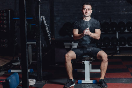 Beautiful handsome young athlete dressed in black t-shirt. During this time, sitting on the tires and applying talcum to your hands in the gym.の写真素材