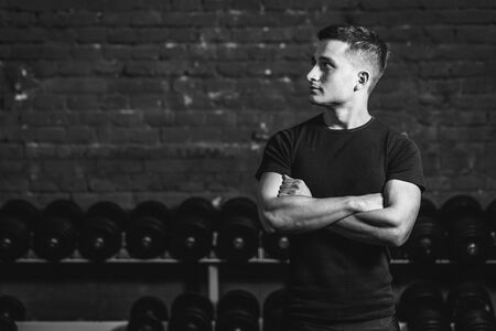 A young athlete is standing in the gym. During this dress, wear a black T-shirt. Standing on a black background and looking away. At the same time placing a hand on his hand.の写真素材