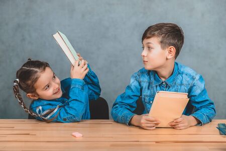 Naughty little schoolboy is hitting lovely schoolgirl in her head with a book. Girl is shielding herself. Fight.の写真素材
