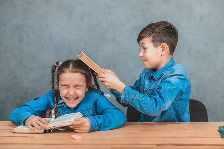 Naughty little schoolboy is hitting lovely schoolgirl in her head with a book. Fight.