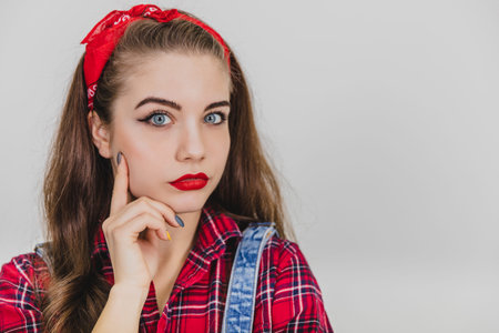 Beautiful young girl in red standing, holding hands near her chin, posing, looking at the camera...