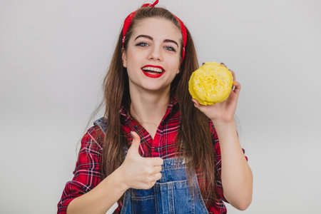 Nice young girl holding a big doughnut with yellow icing, giving her thumb up.