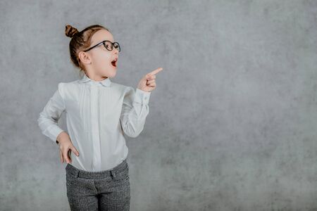 Small business lady in stylish business clothing on a gray background. Dressed in glasses An index finger points to the side. Gray background.の写真素材