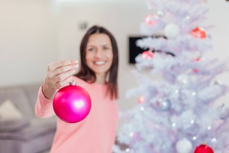 Young woman in a pink sweater holding a Christmas decoration bauble for the Christmas tree, showing off what nice toys she has bought for this christmas.の写真素材