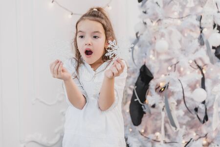 Little girl playing with christmas tree snowflakes whilr decorating a fir.の写真素材