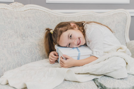 Inspired child daughter woke up on the Christmas morning and is sitting on the sofa hugging a gift.