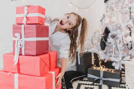 Cute kid prepared a pile of red gift boxes with white ribbons for her friends and family.の写真素材