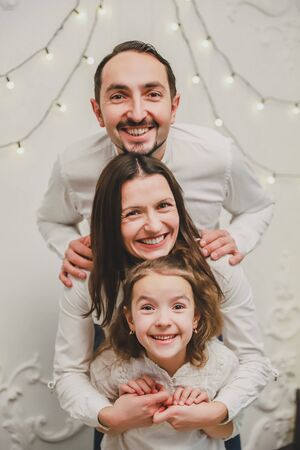 Cute family playing around on Christmas morning, funny father mother and daughter stay in the position where their heads is one above another, like a tower.の写真素材