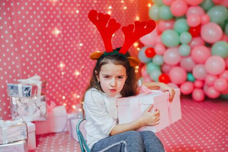 Child, present and sledge on the pink celebration background. Greedy child is frowning, keeping box close to her chest.の写真素材