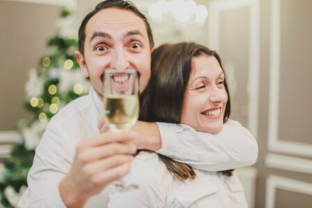 Making fool and entertainment concept. Photo of couple celebrating new year with champange. Childish man put a glass in front of teeth making fun.の写真素材