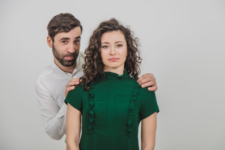 Handsome young man flirting with her woman, embracing her from behind, looking innocently at the...