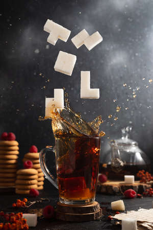 Sugar in the form of tetris figures falls into a glass of tea. Tea splashes upの写真素材