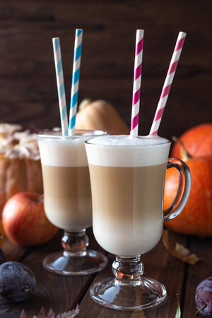 Two glass latte mugs stand on a table. Coffee and milk are poured in layers, tubes with stripes are inserted on top of the drink.の写真素材