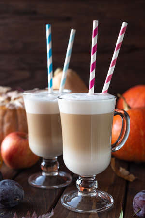 Two glass latte mugs stand on a table. Coffee and milk are poured in layers, tubes with stripes are inserted on top of the drink.の写真素材