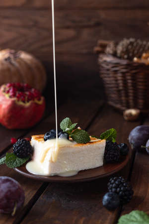 A square piece of cottage cheese casserole lies on a plate, decorated with berries. Condensed milk is poured on top of the omeletの写真素材