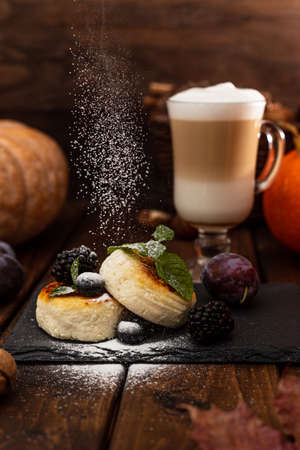 Two cheesecakes and a glass mug with latte stand on a wooden table on a black stand. Powdered sugar is poured on top of the cheesecakesの写真素材