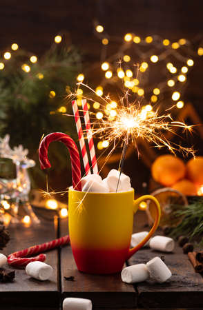A mug of cocoa with marshmallows from which straws stick out, a caramel stick and a burning sparklerの写真素材