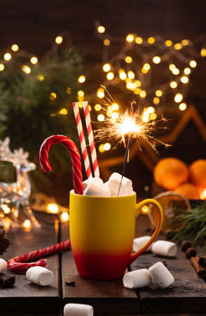 A mug of cocoa with marshmallows from which straws stick out, a caramel stick and a burning sparklerの写真素材