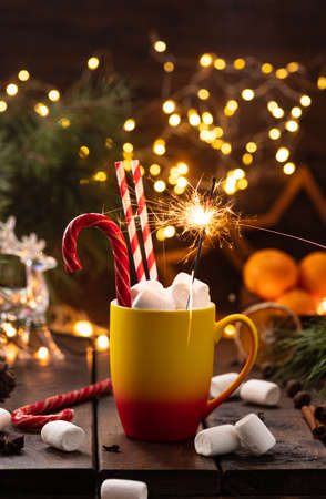 A mug of cocoa with marshmallows from which straws stick out, a caramel stick and a burning sparklerの写真素材