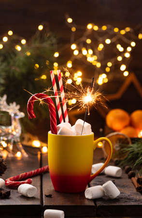 A mug of cocoa with marshmallows from which straws stick out, a caramel stick and a burning sparklerの写真素材