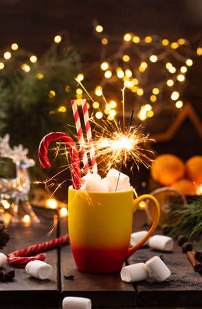 A mug of cocoa with marshmallows from which straws stick out, a caramel stick and a burning sparklerの写真素材