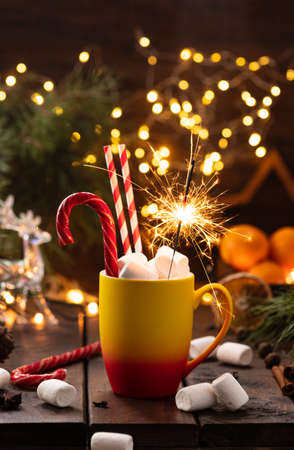 A mug of cocoa with marshmallows from which straws stick out, a caramel stick and a burning sparklerの写真素材