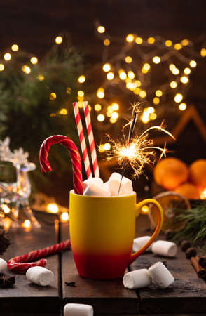A mug of cocoa with marshmallows from which straws stick out, a caramel stick and a burning sparklerの写真素材