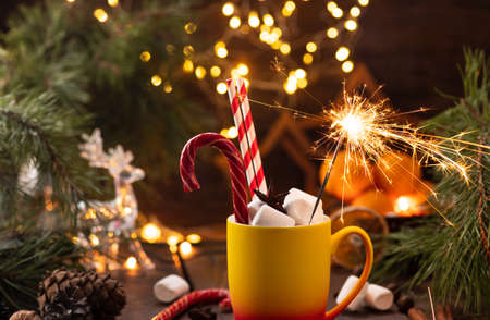 A mug of cocoa with marshmallows from which straws stick out, a caramel stick and a burning sparklerの写真素材