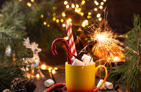 A mug of cocoa with marshmallows from which straws stick out, a caramel stick and a burning sparklerの写真素材
