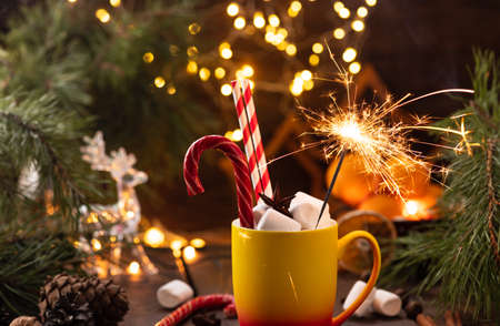 A mug of cocoa with marshmallows from which straws stick out, a caramel stick and a burning sparklerの写真素材