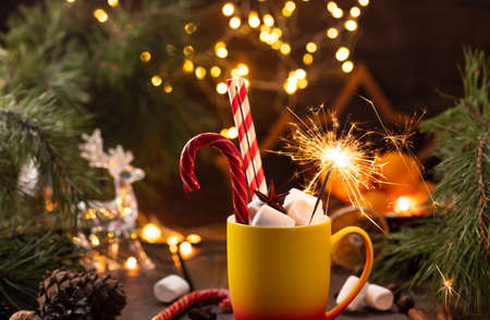 A mug of cocoa with marshmallows from which straws stick out, a caramel stick and a burning sparklerの写真素材
