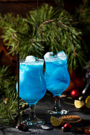 blue cocktail in a tall glass with ice and lemon slicesの写真素材
