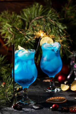 blue cocktail in a tall glass with ice and lemon slices on a wooden backgroundの写真素材