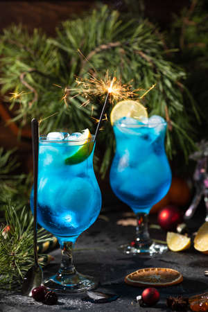 blue cocktail in a tall glass with ice and lemon slicesの写真素材