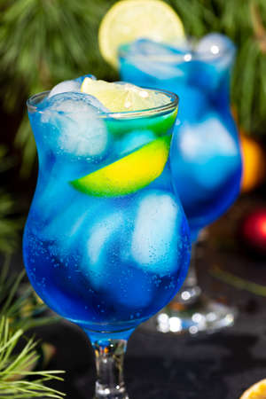 blue cocktail in a tall glass with ice and lemon slicesの写真素材