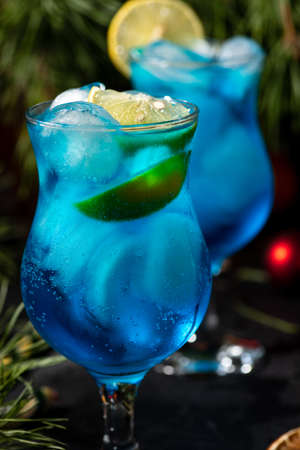 blue cocktail in a tall glass with ice and lemon slices on a wooden backgroundの写真素材
