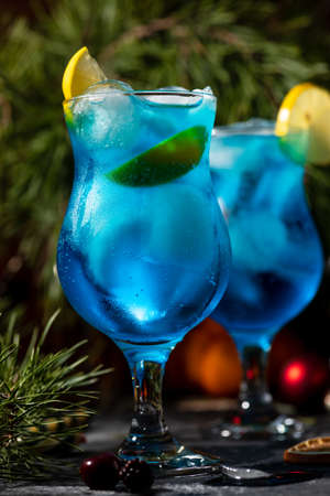 blue cocktail in a tall glass with ice and lemon slices on a wooden backgroundの写真素材