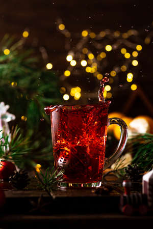 red tea in a glass splashes up due to the fact that a strainer with tea leaves falls into itの写真素材