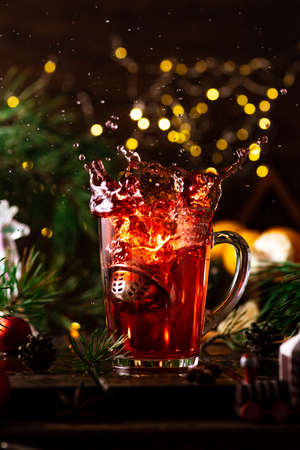 red tea in a glass splashes up due to the fact that a strainer with tea leaves falls into itの写真素材