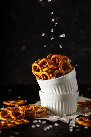 pretzels lie in two cups on a dark background. A large amount of salt is poured on top of the bretzel and scattered around.の写真素材