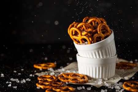 pretzels lie in two cups on a dark background. A large amount of salt is poured on top of the bretzel and scattered around.の写真素材