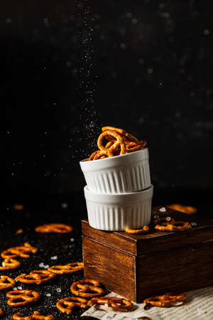 pretzels lie in two cups on a dark background. A large amount of salt is poured on top of the bretzel and scattered around.の写真素材
