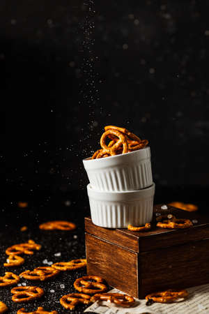 pretzels lie in two cups on a dark background. A large amount of salt is poured on top of the bretzel and scattered around.の写真素材
