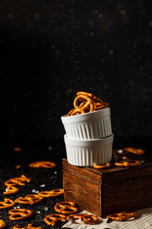 pretzels lie in two cups on a dark background. A large amount of salt is poured on top of the bretzel and scattered around.の写真素材