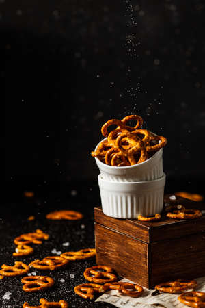 pretzels lie in two cups on a dark background. A large amount of salt is poured on top of the bretzel and scattered around.の写真素材