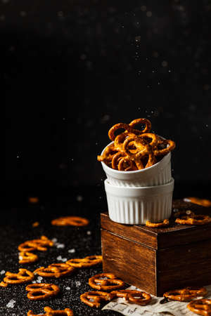 pretzels lie in two cups on a dark background. A large amount of salt is poured on top of the bretzel and scattered around.の写真素材