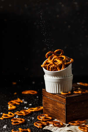 pretzels lie in two cups on a dark background. A large amount of salt is poured on top of the bretzel and scattered around.の写真素材