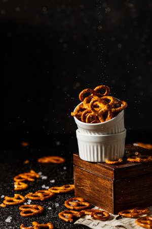 pretzels lie in two cups on a dark background. A large amount of salt is poured on top of the bretzel and scattered around.の写真素材